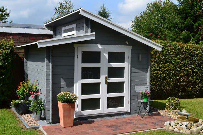 Aktiva-40 ist nicht ohne Grund eines unserer beliebtesten Gartenhaus-Modelle: Mit grau-weißem Anstrich passt es auch perfekt zu roten Terrassen-Fliesen. 