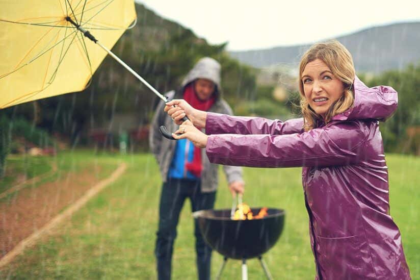 Frau hält Schirm bei Regen beim Grillen