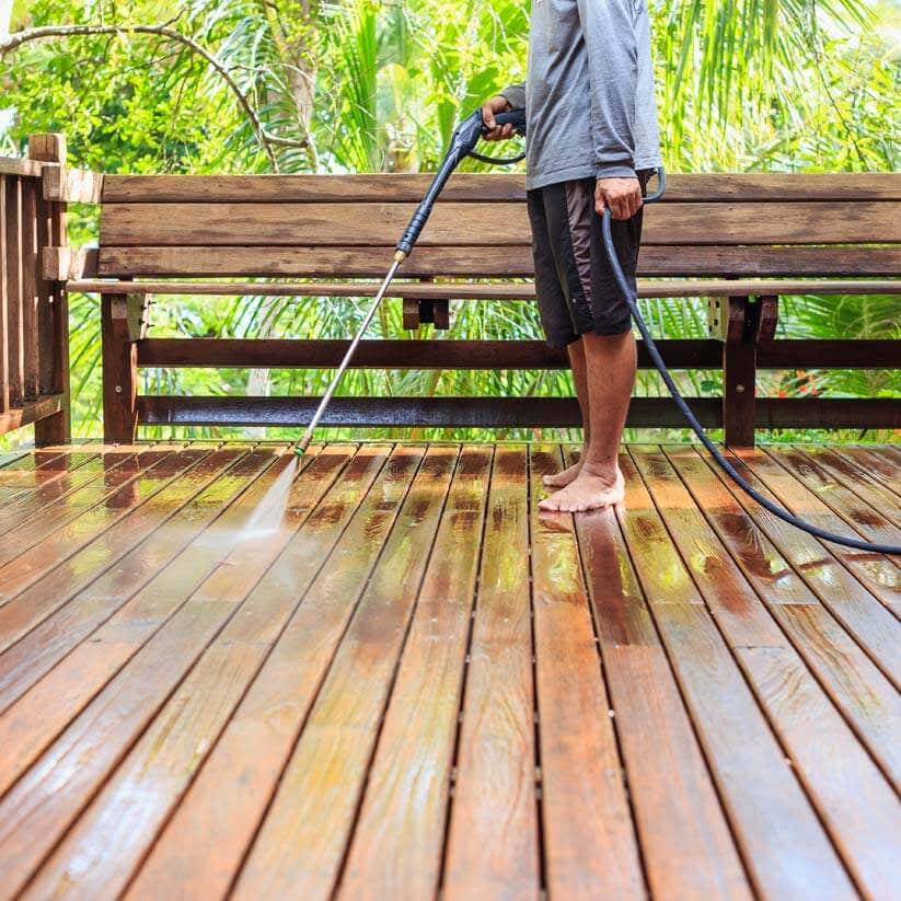 Mann reinigt Terrassen Holzboden mit Wasserstrahl