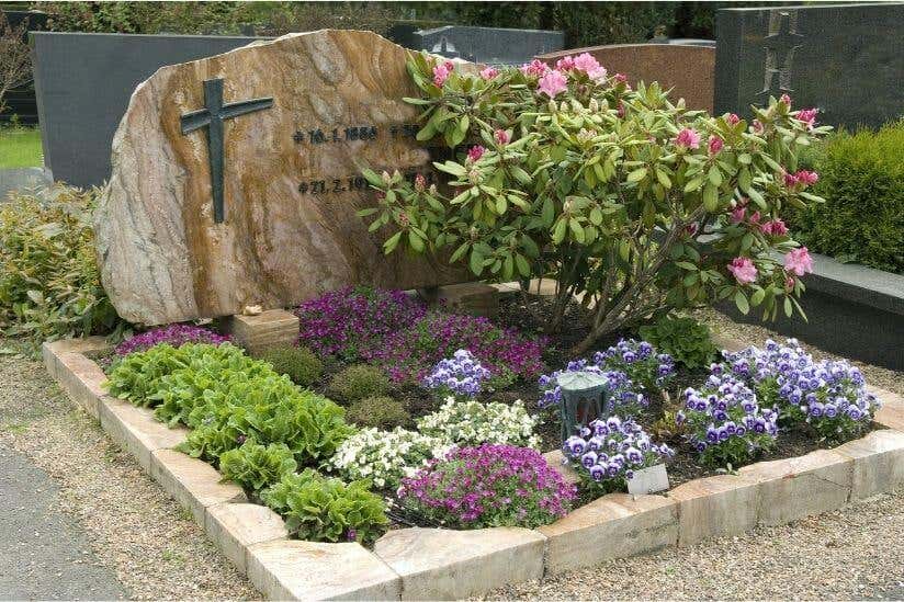 Bunt bepflanztes Grab mit Grabstein