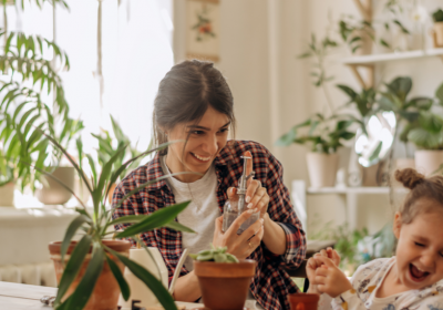 Frau mit einer kleinen Tochter pflanzt Zimmerpflanzen zu Hause und hat Spaß beim Spritzwasser